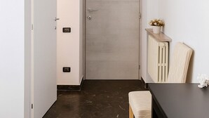 A room with a closed door, a small table with a chair, an air conditioning unit above the door, a radiator, and a wall-mounted hook. - Colosseo Rooms (Rome)