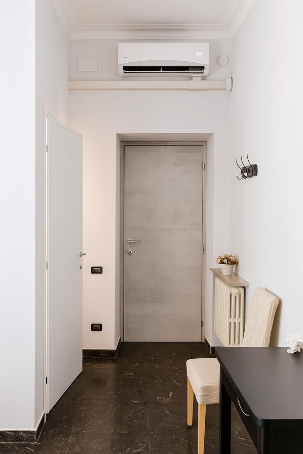 Une pièce avec une porte fermée, un climatiseur fixé au mur, une petite table avec une chaise et un radiateur posé sur le sol.
