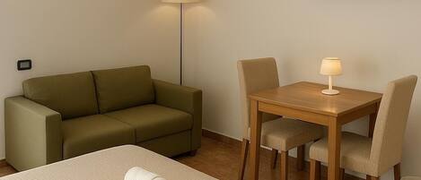 Una habitación de hotel con una cama, un sofá, una mesa de comedor con sillas, un televisor y una lámpara de pie.