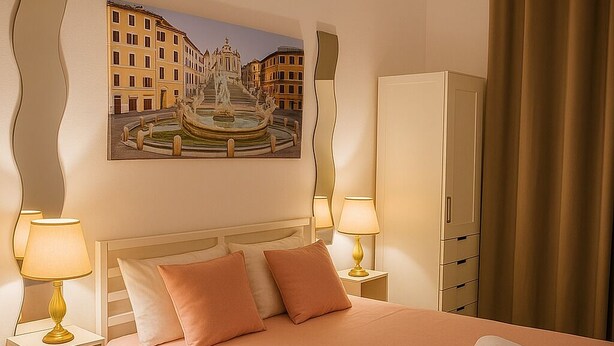 A hotel room with a bed, two bedside lamps, a nightstand, a wardrobe, and a painting of a cityscape. - Colosseo Rooms (Rome)