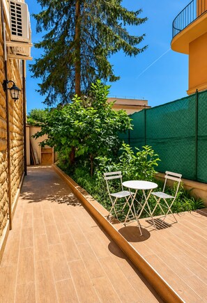 A narrow outdoor corridor with a tiled floor, a green fence, and a small table with two chairs. - Colosseo Rooms (Rome)