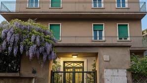 A multi-story building with a gated entrance, balconies, and a wisteria plant. - Colosseo Rooms (Rome)
