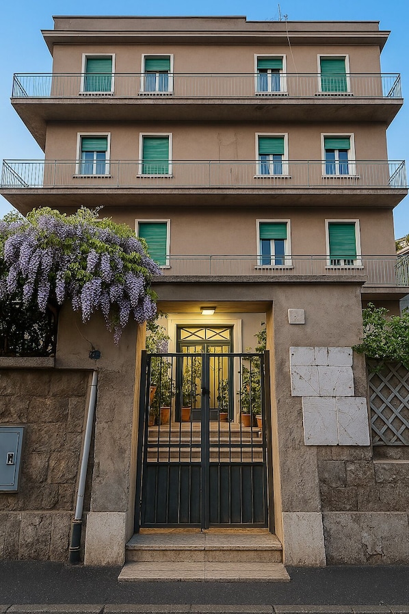 Un edificio a più piani con ingresso carrabile, balconi e un rampicante di glicine.