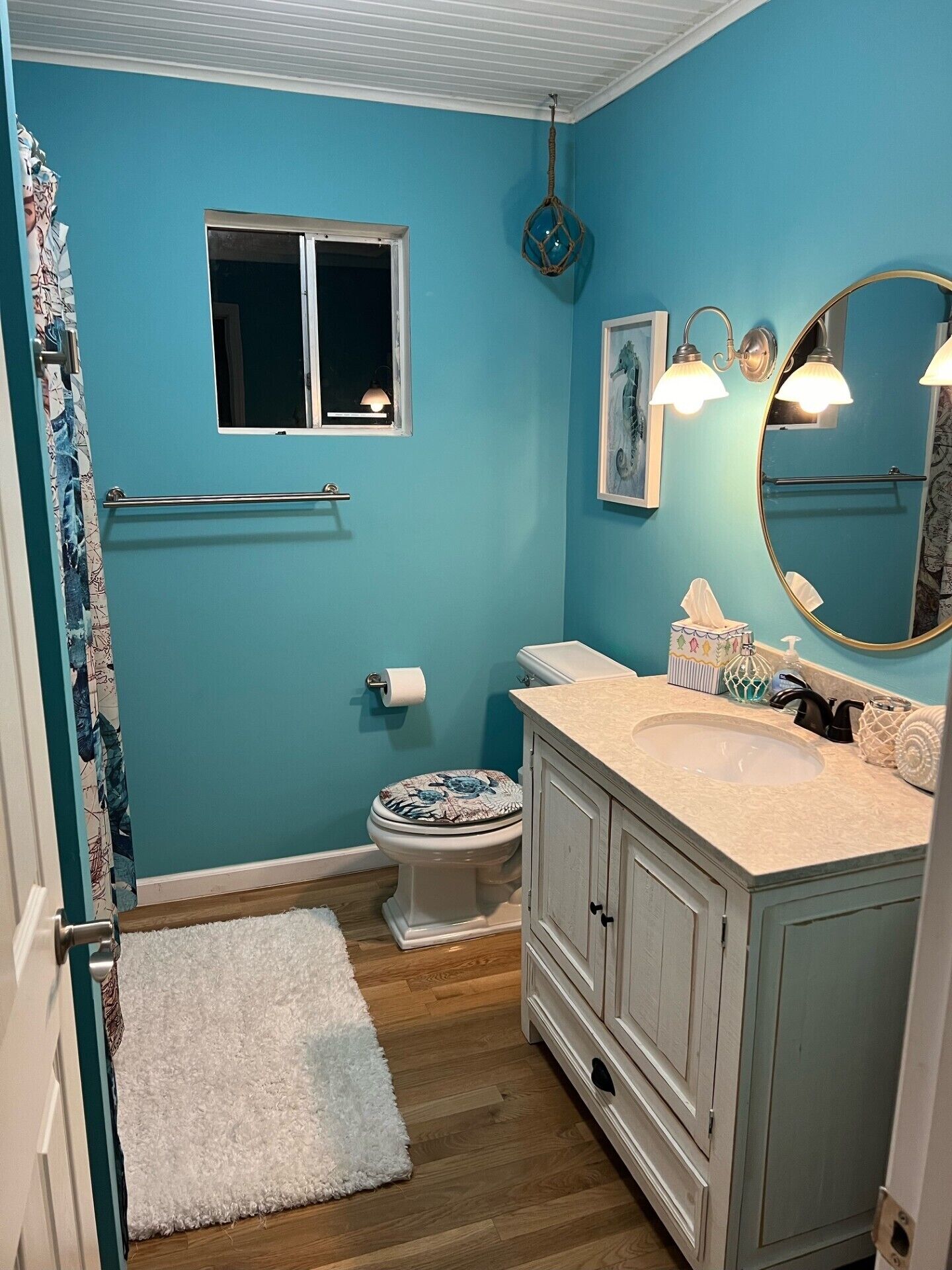 A bathroom with a blue wall, white vanity, and a round mirror.