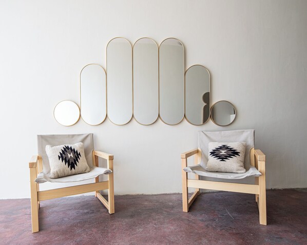 Two wooden chairs with cushions, a wall-mounted mirror, and a concrete floor.
