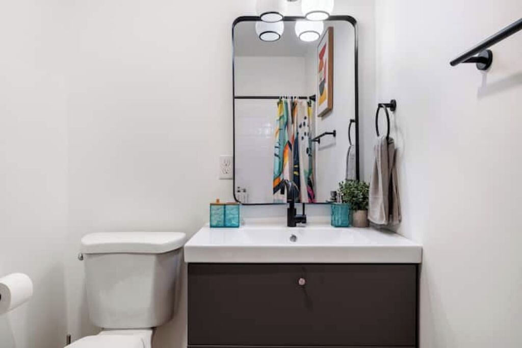 A modern bathroom with a white toilet, a dark vanity, and a mirror above the sink.