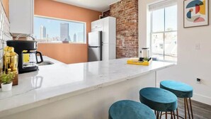 A modern kitchen with a marble countertop, a brick accent wall, and a city view. - Modern 1BR Brick+Kingbed+Free Parking+Close to DT (Pittsburgh)