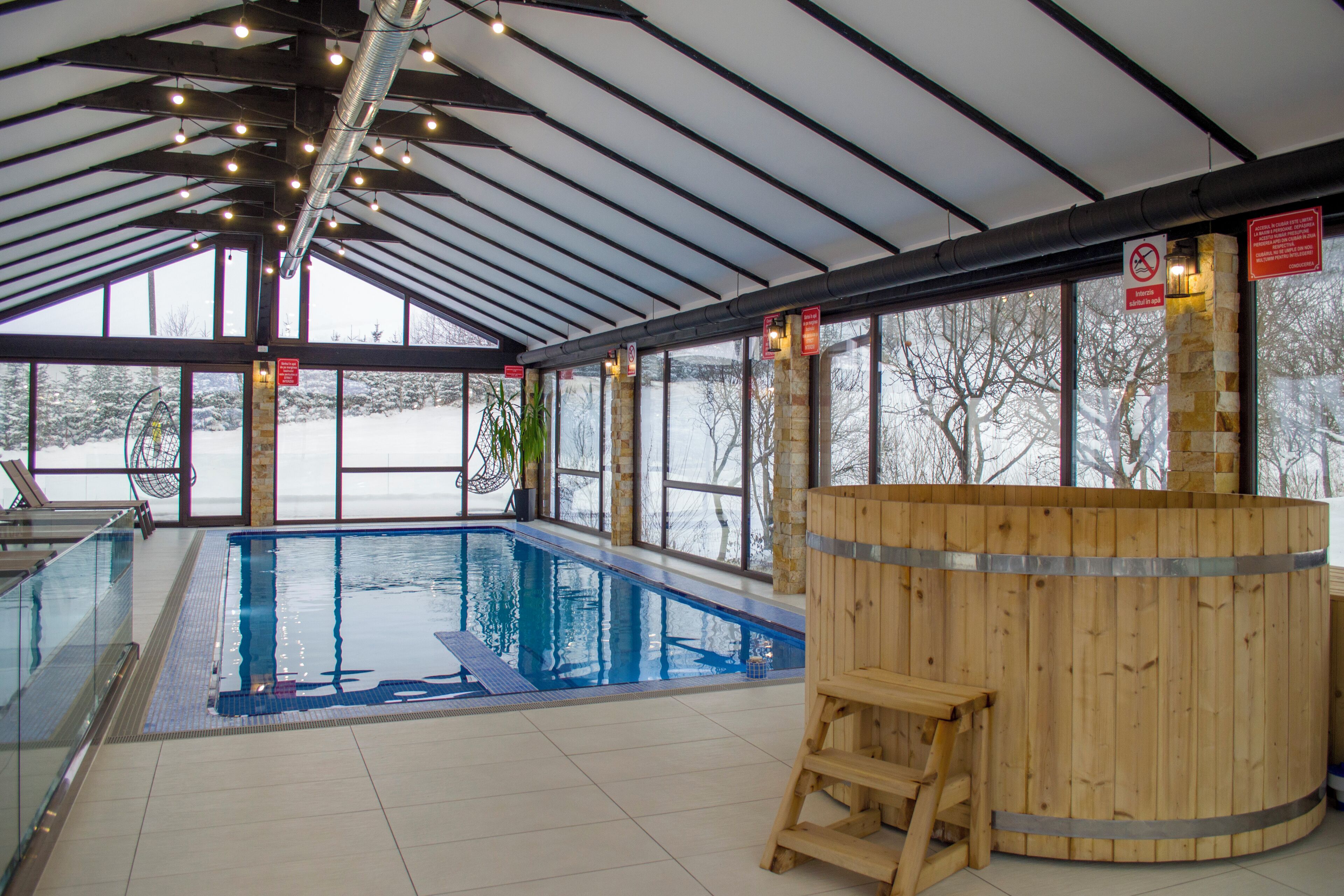 An indoor swimming pool with a wooden sauna, large windows, and a covered roof.