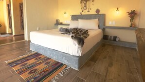 A bedroom with a large bed, a decorative wall hanging, bedside lamps, and a colorful rug. - Casa Jasmin Troncones (Troncones)