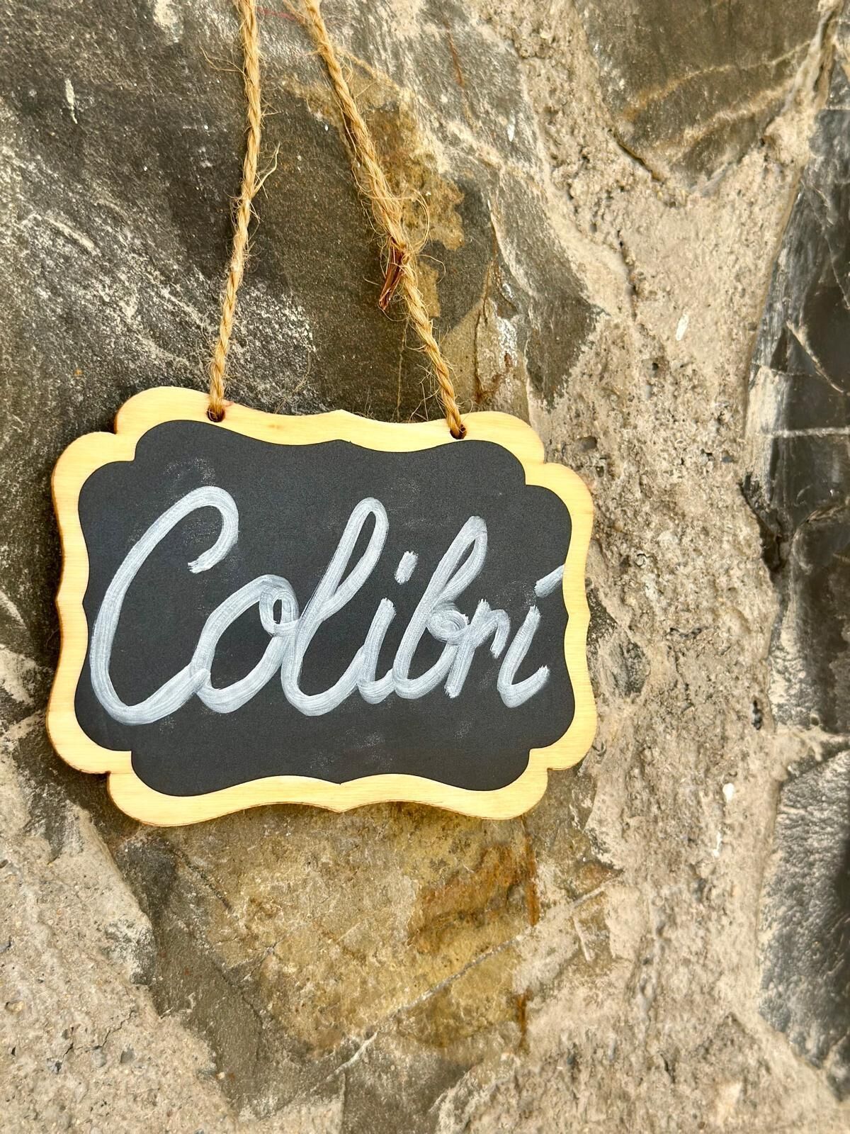 A chalkboard sign with the word "Colibri" written on it, hanging on a stone wall.
