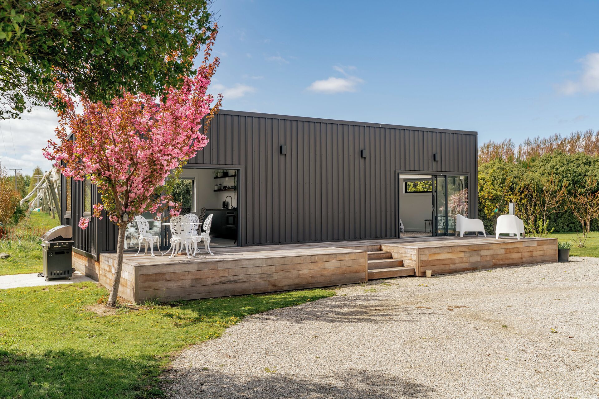 A modern building with a flat roof, a covered outdoor seating area, and a gravel driveway.