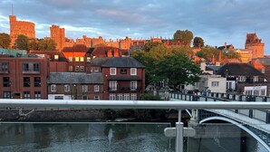 A riverside view with a historic castle in the background, a modern bridge, and a flower arrangement on a table. - The best Windsor Castle and river Thames Panoramic views (Eton)