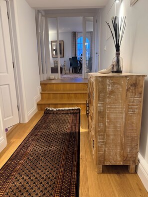 A hallway with a patterned rug, a wooden cabinet, and a staircase leading to a dining area.