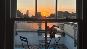 A balcony with a view of the sunset, a table with chairs, and a potted plant. - The best Windsor Castle and river Thames Panoramic views (Eton)