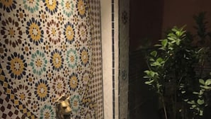 Ett badrum med en vägg täckt av mosaik, ett badkar med en marmorskiva som avställningsyta och en krukväxt.