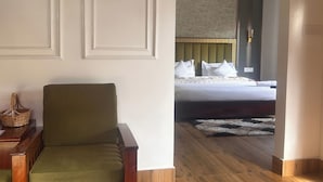 A hotel room with a wooden floor, a green armchair, a wooden side table, and a bed with a headboard and pillows. - Zen Resort (West Kameng)