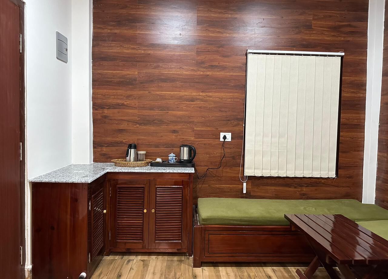 Ein kleiner Raum mit Holzboden, einer Küchenzeile mit Arbeitsplatte und Schränken, einem grünen Sofa und einem Fenster mit Jalousien.