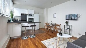 Una cocina moderna con armarios blancos, un taburete de bar y una zona de comedor con mesa y sillas.