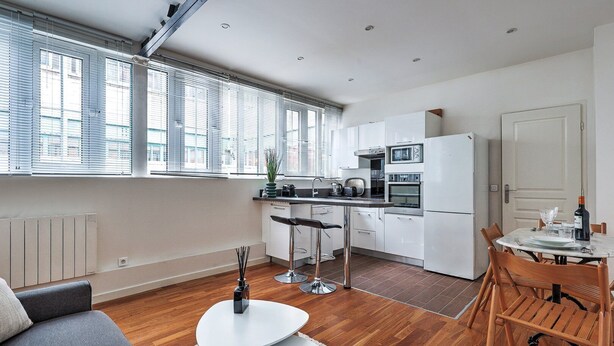 Una cocina moderna con armarios blancos, un microondas y un refrigerador. Hay un comedor con una mesa y sillas.