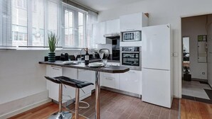Una cocina moderna con armarios blancos, horno empotrado y microondas. Hay un taburete de bar y una planta en maceta sobre la encimera.