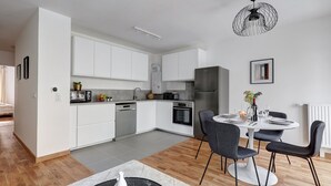 Una cocina moderna con armarios blancos, horno integrado y refrigerador de acero inoxidable.