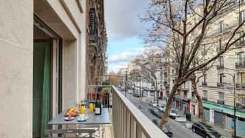 Ein Balkon mit einem Frühstückstisch, mit Blick auf eine Straße mit parkenden Autos und Gebäuden.