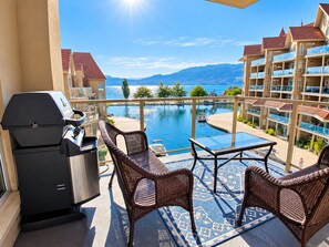 A balcony with a grill, wicker chairs, and a view of a swimming pool and mountains.
