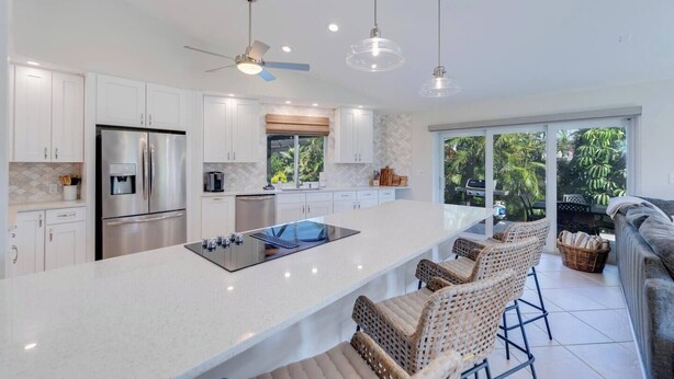 A modern kitchen with a central island, stainless steel appliances, and a dining area with wicker chairs. - Sea Suite (Marco Island)