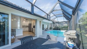 A covered outdoor area with a pool, a grill, and a table with chairs. - Sea Suite (Marco Island)