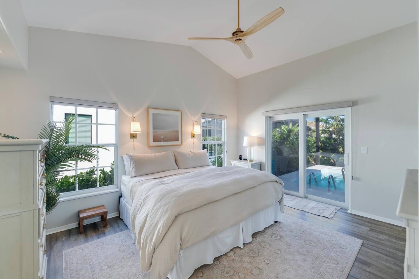 A bedroom with a bed, a ceiling fan, a window, and a view of a pool.