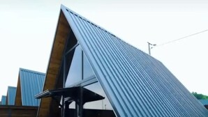 Una terraza con jacuzzi, sillones de madera y un edificio moderno con techo inclinado.