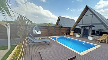 A modern outdoor pool area with a wooden deck, a hanging chair, and a lounge chair.