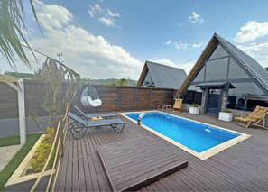 A modern outdoor pool area with a wooden deck, a hanging chair, and a lounge chair. - Club Armada Bungalov (Sapanca)