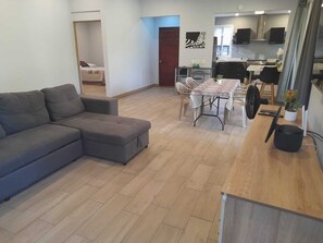 A modern living room with a grey sectional sofa, a dining area with a table and chairs, and a kitchen with cabinets and a stove. - Charming 2-bedroom house with WiFi, AC in adorable Las Isletas (Las Isletas)
