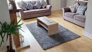 A living room with two sofas, a coffee table, and a large window with curtains. - 3 bedroom accommodation in Conwy (Conwy)