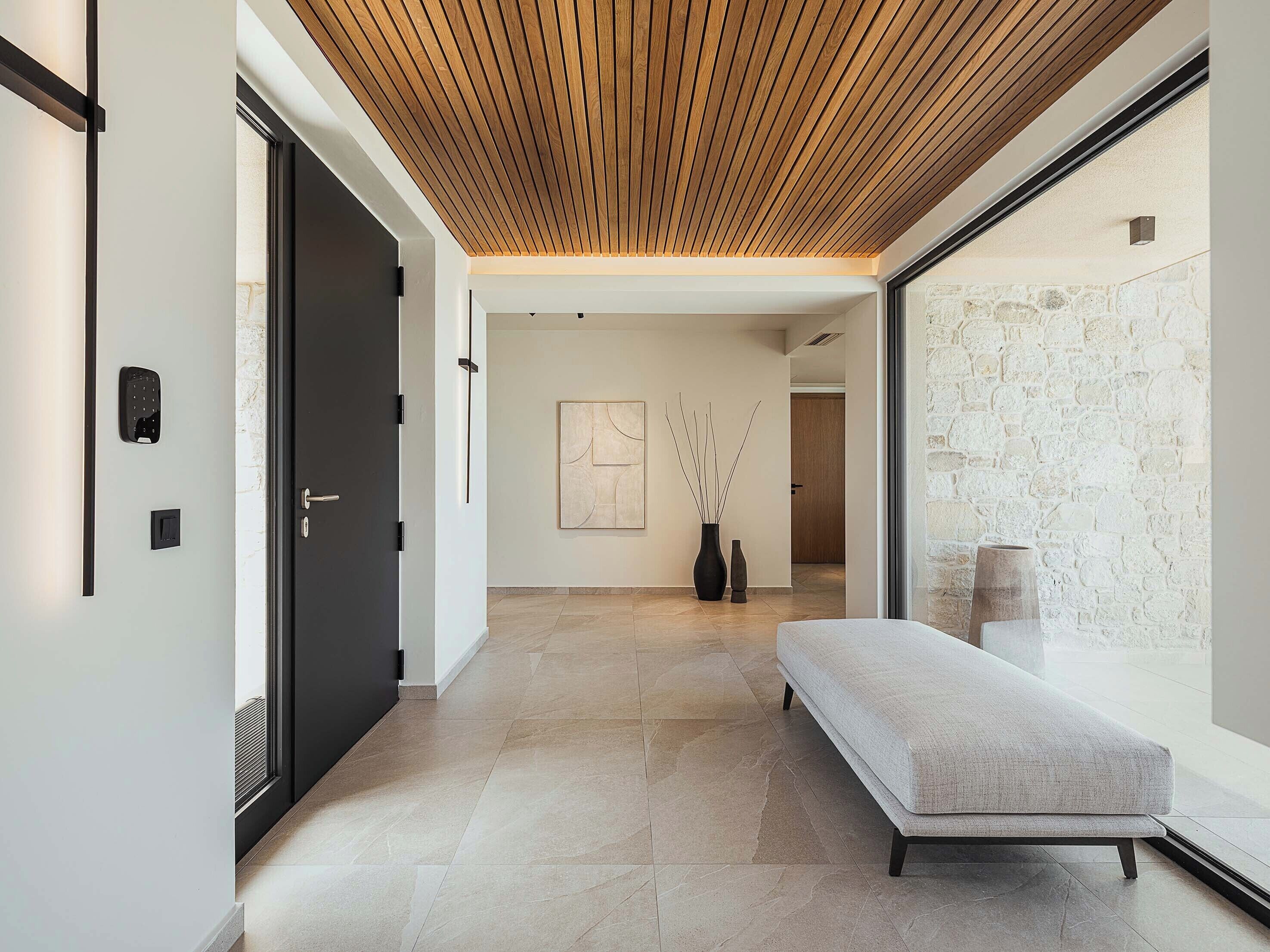 A modern hallway with a wooden ceiling, a bench, and a stone wall.