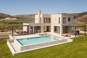 A modern two-story house with a swimming pool, outdoor seating, and a view of the surrounding landscape.