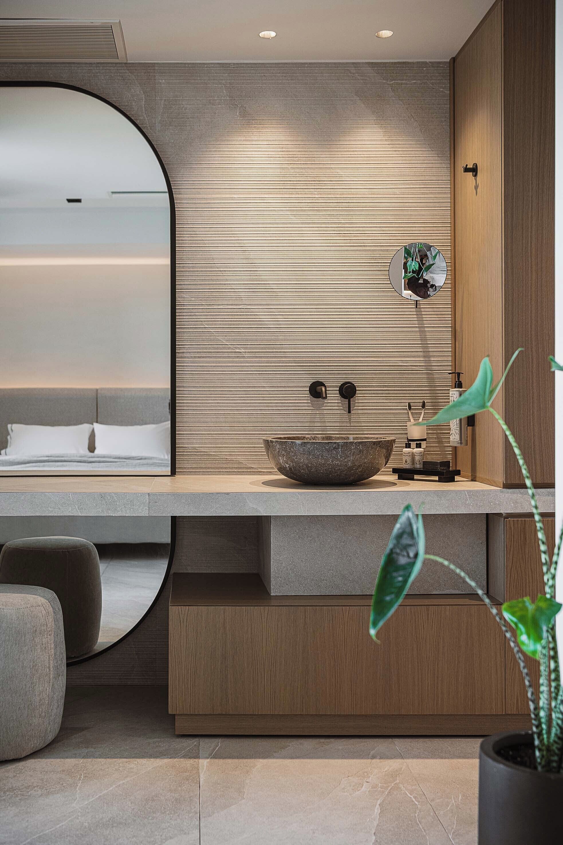 A modern bathroom with a large round mirror, a wooden vanity, and a large bowl sink.