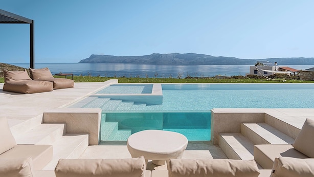 Ein moderner Poolbereich im Freien mit freiem Blick auf das Meer und die dahinterliegenden Berge.