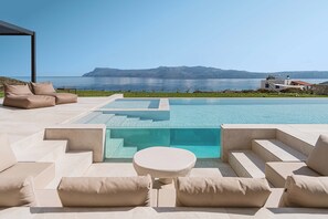 A modern outdoor pool area with a clear view of the sea and mountains in the background.