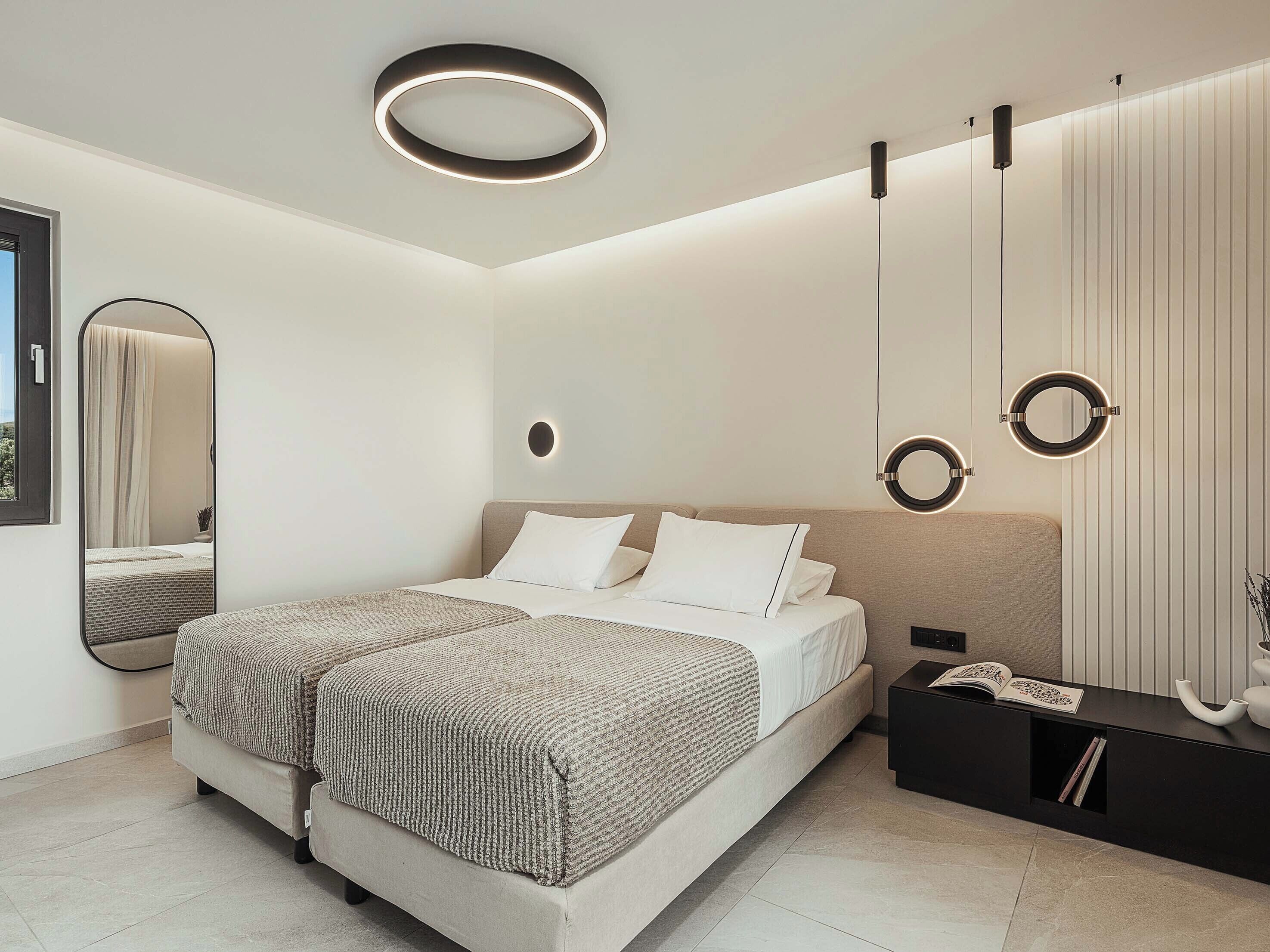 Un dormitorio moderno con una cama grande, una mesita de noche, un espejo y una lámpara de pared.