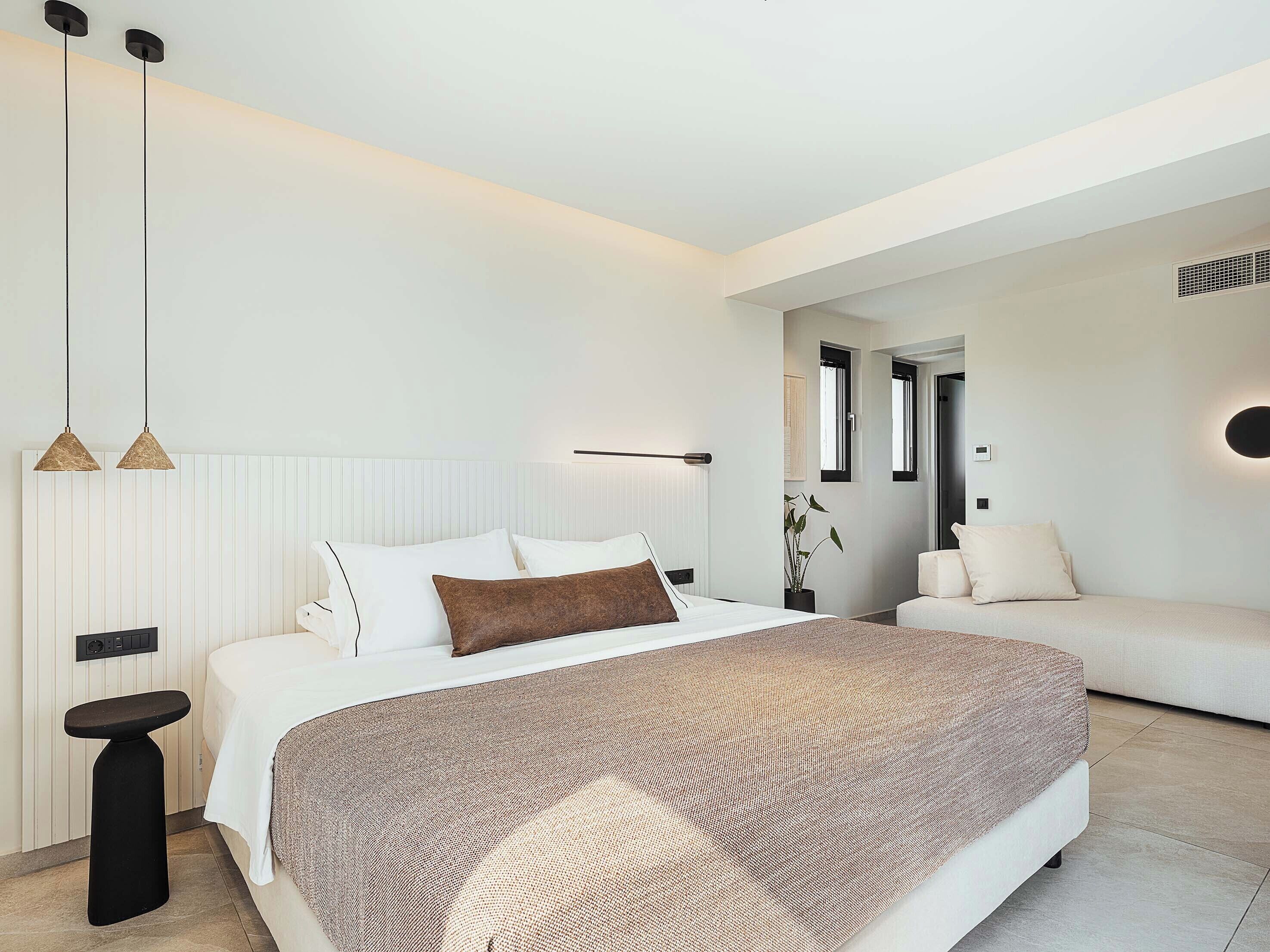 Ein modernes Schlafzimmer mit einem großen Bett, Nachttischen, einer Couch und Pendelleuchten.