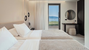 Ein Hotelzimmer mit Bett, Nachttisch, Spiegel und Meerblick durch eine Glastür.