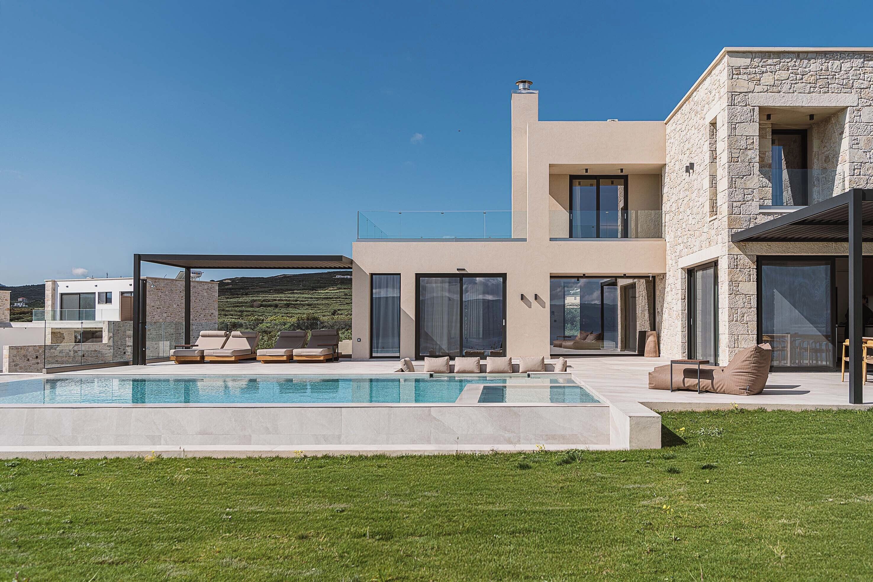Une maison moderne à deux étages, dotée d’une piscine, d’un espace salon extérieur et de grandes fenêtres.