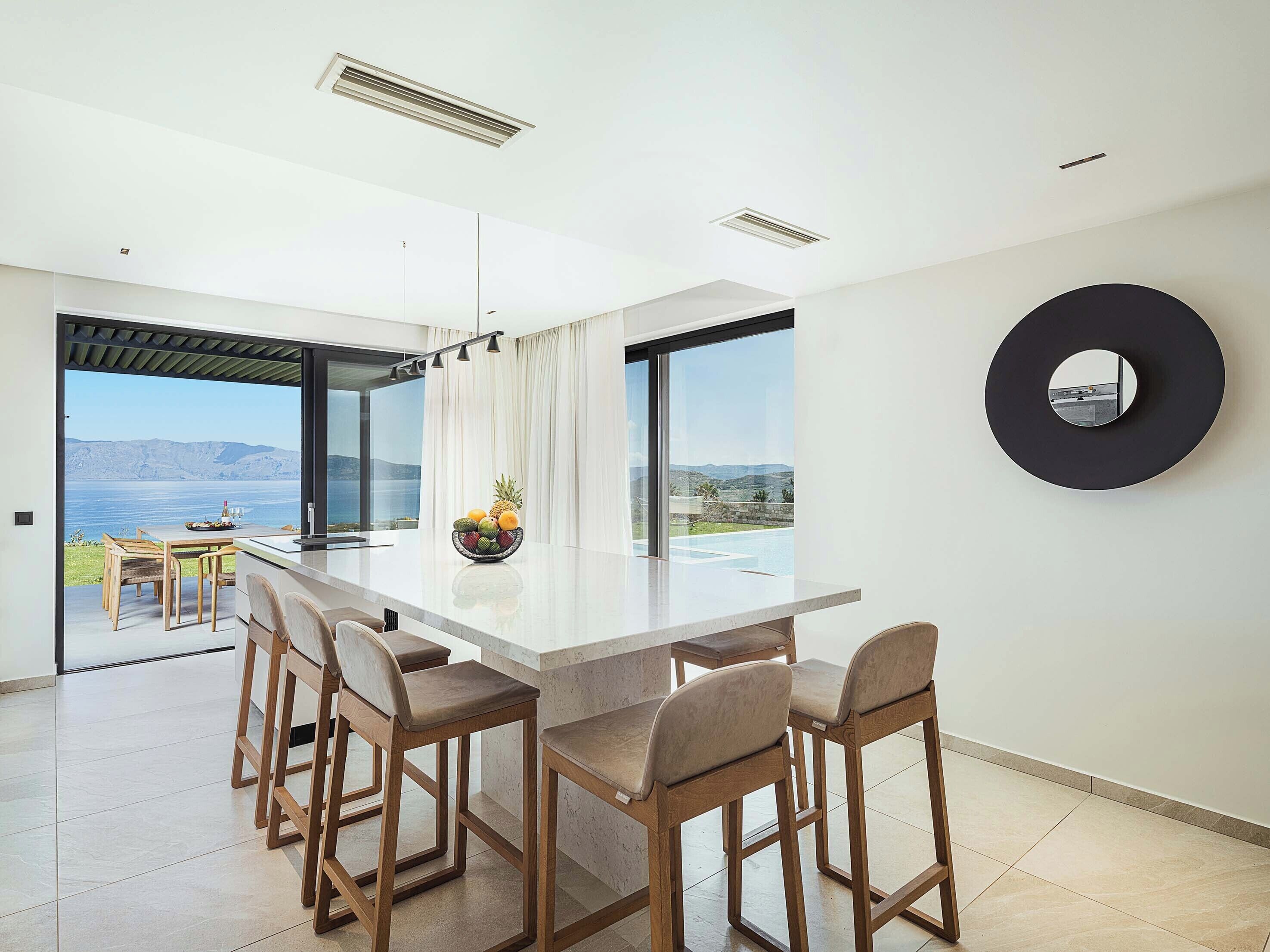 A modern kitchen with a large island, bar stools, and a view of the sea.