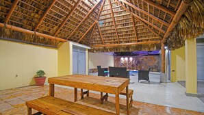 Un espacio interior con techo de paja, muebles de madera y piso de baldosas.