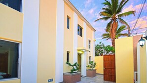 Un edificio moderno con fachada amarilla, ventanas amplias y una palmera al fondo.