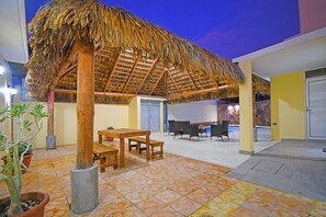 Relax under the thatched-roof structure, surrounded by lush greenery and comfortable seating.