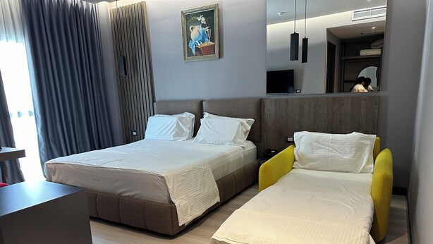 A hotel room with two beds, a desk, a mirror, and a painting on the wall. - HOTEL OLIVE (Vlorë)