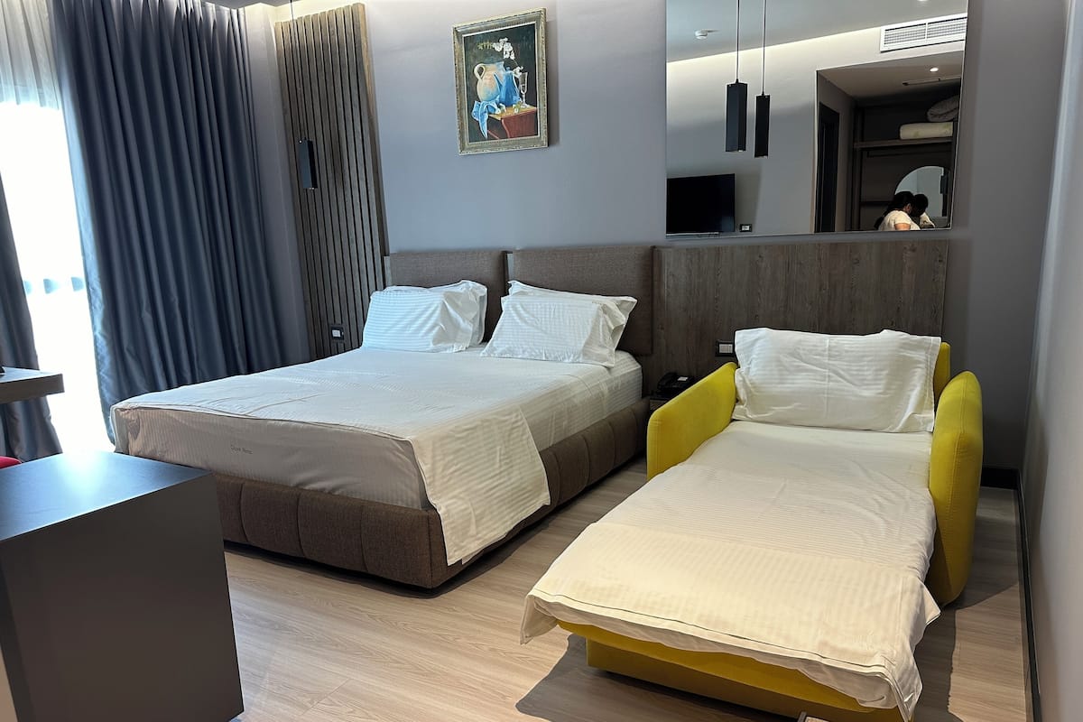 A hotel room with two beds, a desk, a mirror, and a painting on the wall.